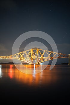 Scenery of the famous Forth Rail Bridge illuminated by night lights reflected in water in Scotland