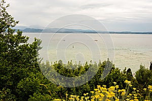 Scenery of Lake Garda over trees with a beautiful landscape in the background in Sirmione, Italy.