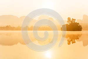 Scenery landscape of tropical lake in the morning mist, golden sun shining down on the lake and mountain range backdrop