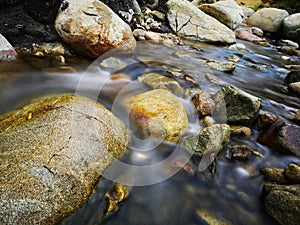 Scenery of river stream flowing between rocks with motion blur due to slow shutter effect and selective focus.