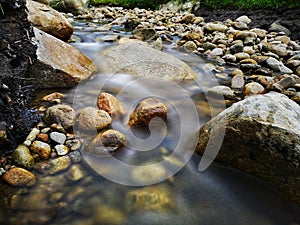Scenery of river stream flowing between rocks with motion blur due to slow shutter effect and selective focus.
