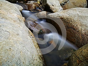 Scenery of river stream flowing between rocks with motion blur due to slow shutter effect and selective focus.