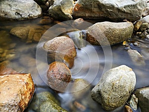 Scenery of river stream flowing between rocks with motion blur due to slow shutter effect and selective focus.