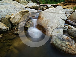 Scenery of river stream flowing between rocks with motion blur due to slow shutter effect and selective focus