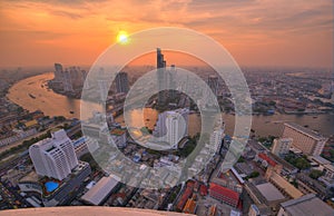 Scenery of sunset sky reflected on Chao Phraya River in Bangkok with Taksin Bridge over the river and skyscrapers along riverside