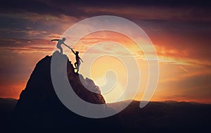 Scenery view with a team of two climbers on the top on the mountain. Person helping another to overcome obstacles and reach the