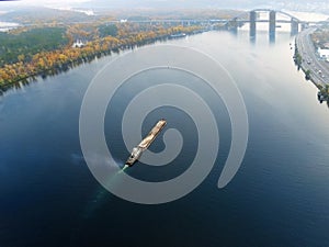 Scenic aerial cityscape of Kiev and river Dnipro at sunset. Tugboat supporting barge with sand bulk materials heading down river