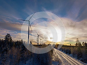 Scenic aerial photo over forest winter road with windmills standing in row at the left side in forest. Road at the right side