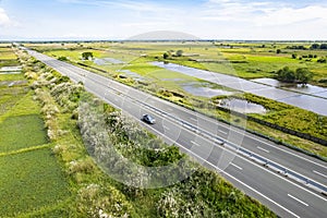 Scenic aerial shot of an empty highway cutting through lush green fields under a clear blue sky, emanating tranquility and ease.