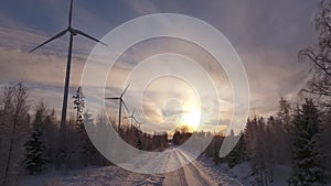 Scenic aerial video over forest winter road with windmills standing in row at the left side in forest. Large wind turbines