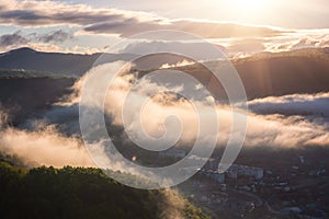 Scenic aerial view of the foggy Carpathian mountains, village and blue sky with clouds in morning light, summer rural landscape