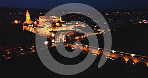 Scenic aerial view of lighted Roman bridge across Guadalquivir river and Mesquite-Cathedral on background with Cordoba