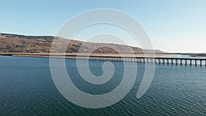 A scenic areal sideway left to right footage of the Barmouth bridge viaduc Wales with majestc mountains and blue water under a