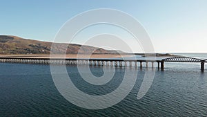 A scenic areal sideway right to left footage of the Barmouth bridge viaduc Wales with majestc mountains and blue water under a