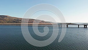 A scenic areal sideway right to left footage of the Barmouth bridge viaduc Wales with majestc mountains and blue water under a