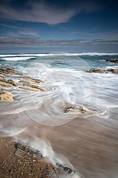 Scenic atlantic coastline with waves in motion around rocks on sandy beach in long exposure, bidart, basque country, france