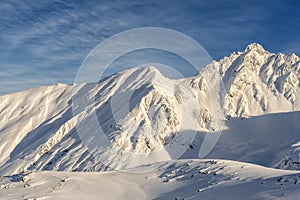 Scenic austrian alpine mountain peaks covered with snow layer in winter at warm sunset or sunrise time. Blue clear sy on