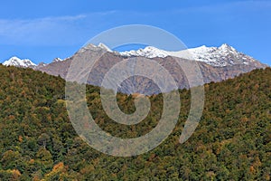 Scenic autumn landscape of Main Caucasus ridge with snowy mountain peak tops on blue sky background