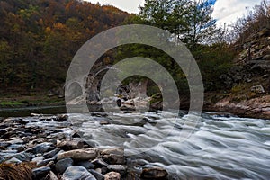 Scenic autumn landscape shot in Bulgarian mountain with ancient bridge and smooth river