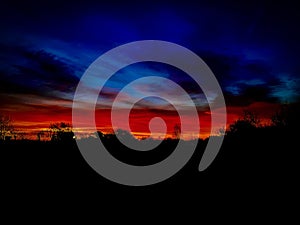 Scenic cloudscape of blue and red sky with silhouettes of trees in Grand Union Canal, Milton Keynes