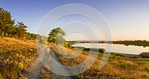 Scenic countryside landscape with rural dirt road across a meadow with dry grass and hay under a clear blue sky. Autumn panorama