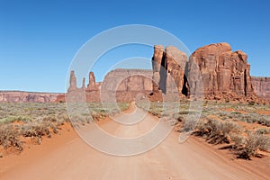 Scenic Dirt Road in the Dry Desert with Red Rocky Mountains in Background.