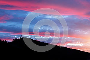 Scenic dramatic fiery cloudy sunset evening view over mountain resort village Bukovel in Ukraine with pine forest christmas tree