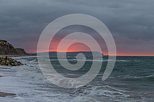 A scenic and dramatic sunset over a choppy sea with dark black thundery sky