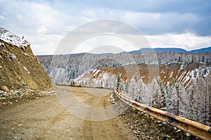 Scenic early spring view with snowy dirt road through the pass, green larch trees, snow and forest on the slopes against