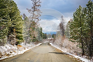 Scenic early spring view with snowy dirt road through the pass, green larch trees, snow and forest on the slopes against