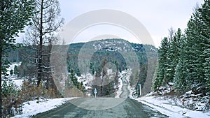 Scenic early spring view with snowy dirt road through the pass, green larch trees, snow and forest on the slopes against