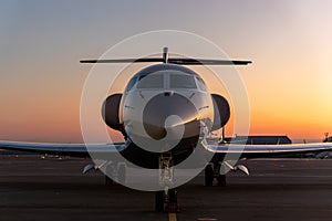 Scenic front view modern luxury expensive private jet plane parked airport taxiway hangar warm colorful dramatic evening