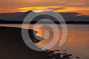 Scenic golden sea sunset with dark volcano in distance island with colorful orange heaven reflection in water, high contrast.