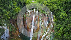 Scenic high waterfall cascading over lush green cliff in dense forest. Mountain stream with clear water.