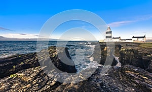 Scenic Hook Lighthouse on rugged cliffs with blue sky, Country Wexford, Ireland