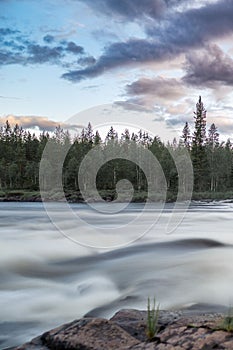 Scenic landscape of a rushing river with rocks and trees in the background in Norrland