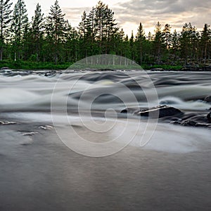 Scenic landscape of a rushing river with rocks and trees in the background in Norrland photo