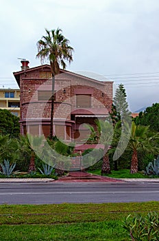 Scenic landscape view of redbrick building is surrounded by palm trees. Stone Hut in a traditional style.