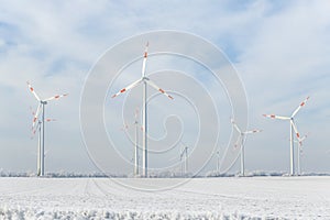 Scenic landscape view of white snowy frosty field and big modern wind turbine mill farm against beautiful blue clouds
