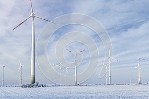 Scenic landscape view of white snowy frosty field and big modern wind turbine mill farm against beautiful blue clouds