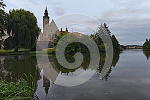 Scenic morning landscape of old Telc castle with brick tower. Buildings reflected in calm water in the lake