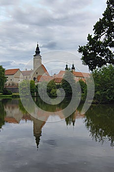 Scenic morning landscape of old Telc castle with brick tower. Buildings reflected in calm water in the lake