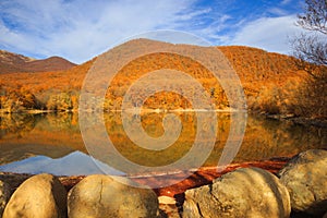 Scenic mountain lake with autumnal forest and big stones along t