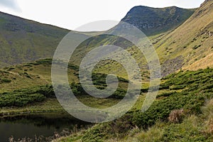 Scenic mountain lake with green grass and blue sly. Natural pond in hills. Countryside and valley background.