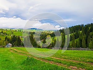 Scenic mountains nature and an old village of wooden cabins on the hills. Sunny spring day with green grass, flowering meadows and