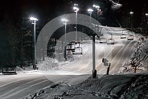 Scenic night view of illuminated snowy ski track with chair ski lift. Night skiing service at Sochi Gorky Gorod winter mountain re