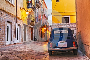 Scenic oldtown street and small retro blue car in Barletta city, Italy