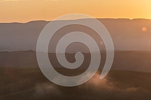 Scenic panorama of the Tuscan landscape with hills and harvest fields in golden morning light, Val d'Orcia, Italy.