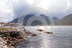 Scenic panorama view of evening ripple sea and mountains in the distance from the rocky shore, where wooden fish dryers are placed