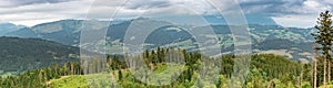 Scenic panorama view of the mountain landscape, forests, pastures, meadows and small villages with a cloudy sky covering the Alps.